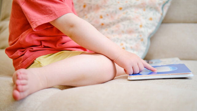 The cute baby is playing with the colorful picture book, flipping through the pages and touching the pictures. The little child reads book. Kid aged about two years (one year ten months)