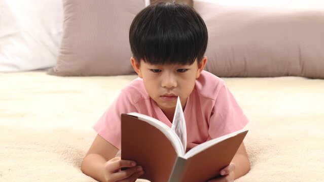 Asian handsome boy reading favorite book while lying down on bed at home, happy little kid spend time free to their advantage. Son enjoying  reading manga new story. staying at home in self isolation.