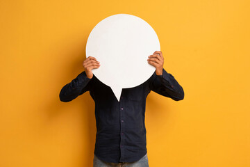 Unrecognizable young man in black shirt hiding face behind empty speech bubble