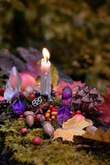 autumn background. Candle with amulet, crystals, fall leaves, fruits, berries, nuts in forest,...