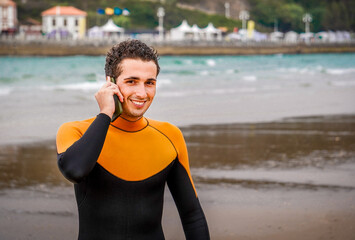 Wet Surfer with Water Drops and Orange Neoprene Holding His Mobile Phone to His Ear on the Beach
