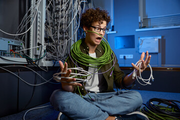 Shocked teenager geek wrapped in wire sitting on floor in data center