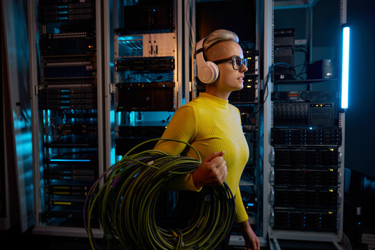 Young woman IT technician walking with wires through server rack in data center