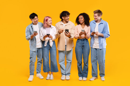 Multiracial friends sharing media content on phones, young diverse people using smartphones over yellow background