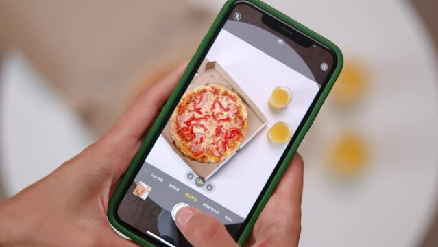 Close up of female hands making photos on modern smartphone of cardboard with pizza and two orange juices. Person photographing food for posting pictures in social media