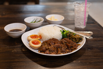 Pork leg rice served in a white plate on a wooden table in a restaurant