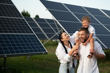 A wide shot of a happy family standing together and smiling at camera with a large solar panel in...