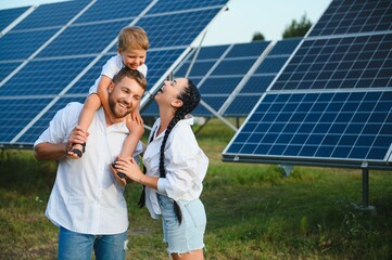 Young family with a small child in her arms on a background of solar panels. A man and a woman look...