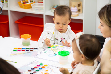 Toddler painting on a white paper in kindergarten