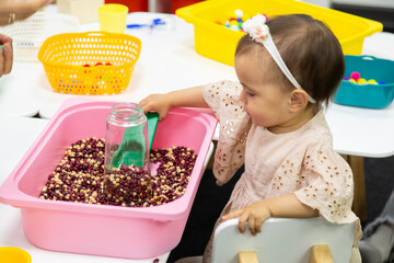 Toddler playing sensory game with bowl of red beans - obrazy, fototapety, plakaty
