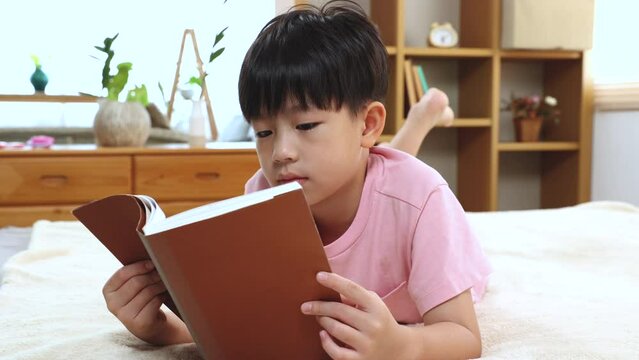 Asian handsome boy reading favorite book while lying down on bed at home, happy little kid spend time free to their advantage. Son enjoying  reading manga new story. staying at home in self isolation.