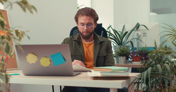 Serious focused businessman work e in office using laptop makes notes, paperwork, guy making urgent deadline task at modern workplace, student study online, rewrite important information startup ideas