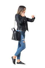 Side view of busy casual fashion girl on the phone checking time on her watch. Full body length...