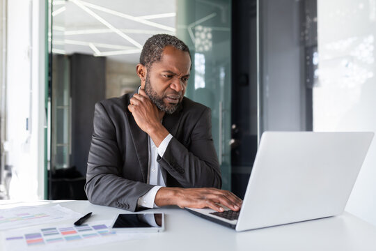 Mature senior thinking businessman at workplace inside office, african american gray haired boss working with laptop inside office.