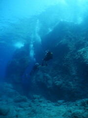 Fototapeta na wymiar scuba divers exploring around a reef underwater deep blue water big rocks and bubbles ocean scenery 