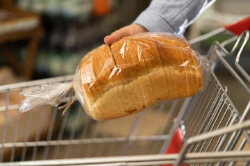 Rollo Brot Close-up of a supermarket shopping trolley and a woman's hand putting a package of sliced bread into it.  © Andrii Lysenko