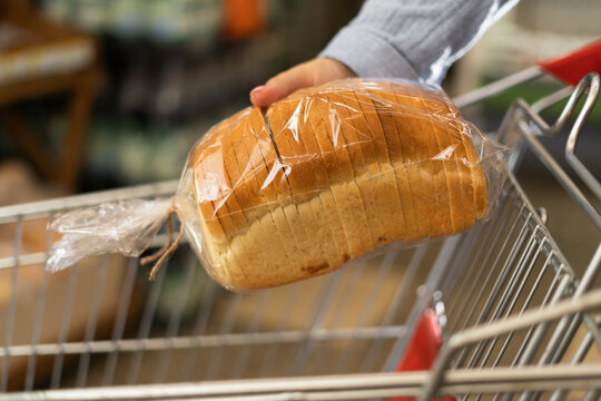 Close-up of a supermarket shopping trolley and a woman's hand putting a package of sliced bread into it.