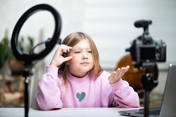 A beautiful blonde teenager is broadcasting live. The video blogger has a live broadcast. An annular lamp and a camera during a live broadcast of a video blogger