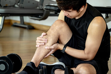 Sport injury concept. Asian male athlete sitting on the floor feeling lower leg cramp. Sport man...
