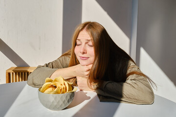 A girl eats crispy potato chips from a bowl on the couch. Quick snack. Calories and diet