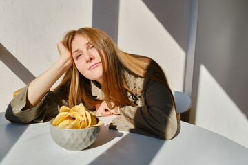 A girl eats crispy potato chips from a bowl on the couch. Quick snack. Calories and diet
