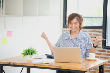 Beautiful young teen Asian business woman using computer laptop with hands up in winner is a gesture, Happy to be successfully celebrating achievement success.