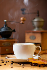 A white cup with a saucer and a number of sprinkled coffee beans and over a cup of steam. Still life in vintage style. Manual coffee grinders.