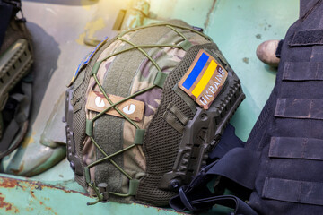 A military helmet of a Ukrainian soldier with a bulletproof vest on an armored car. The flag of...