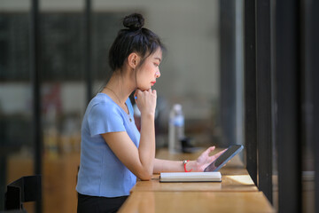 Fototapeta premium A young Asian woman sitting in a coffee shop using her smartphone to search for information inspires new ideas.