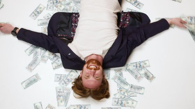 A young rich entrepreneur who won a start-up project lies on the floor in the rain of money. Happy male businessman.