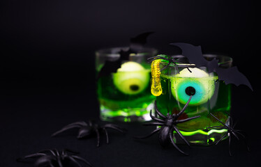 Creepy green cocktails with eyes, jelly worms in a glass and spiders and bats on a black background. Festive Halloween party. Copy space. Close-up. Selective focus.