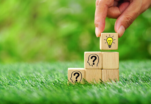 Hand arranging wooden blocks stacking as human head symbol with question mark and yellow light bulb icon on natural environment background.Creative idea and innovation concept.
