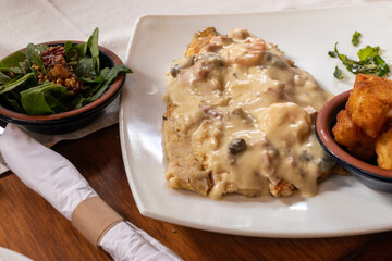 trucha con salsa de champiñones sobre un plato blanco y una ensalada fresca de espinaca y nueces 