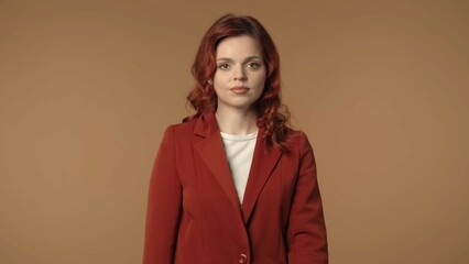 Obraz premium Medium isolated shot of a serious and calm young business woman standing in front of brown background, looking straight at the camera.
