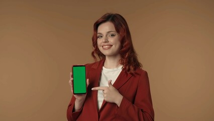 Medium isolated shot of a young woman smiling at the camera and pointing at the phone with advertising area, workspace mock up.