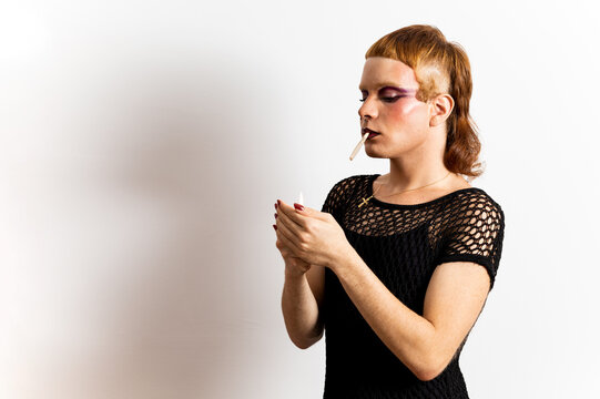 A red-haired non-binary person is posing on a white background with extravagant clothing. The man lights a cigar with a lighter. Concept of people is not identified with any gender.Copyspace. - Powered by Adobe