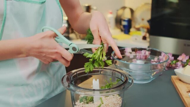 Woman chopping dill with scissors into blender bowl. Close-up of a table. Cooking in the kitchen