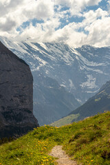Fototapeta premium Trail Leading Down the Swiss Alps in Switzerland in the Summer with Mountains Peaking Through Clouds in the Background
