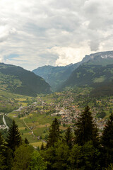 Buildings Sitting Along a Hill of the Swiss Alps in Switzerland in the Summer with Mountains Peaking Through Clouds in the Background