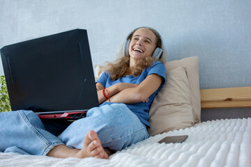 Funny cute teenage girl is lying on the bed and watching videos using a laptop. Chat with friends...