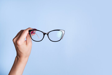 Eyeglasses in female hand on blue background. Optical store, vision test, stylish glasses concept
