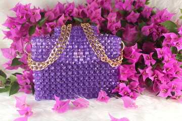 Handmade purple purse made with bright beads on white furry blanket with pink bougainvillea flower....