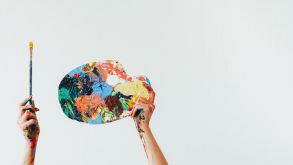 Painter equipment. Drawing tools. Woman artist hands holding colorful messy palette and paintbrush...