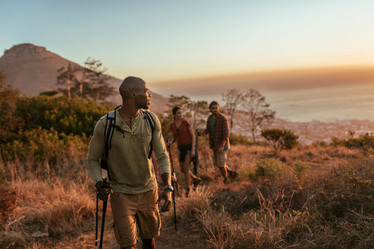 Young and diverse group of people and hikers hiking on a ridge overlooking the ocean and a beautiful sunset in South Africa
