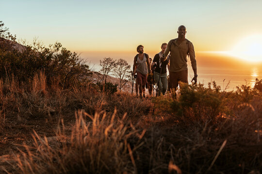 Young and diverse group of people and hikers hiking on a ridge overlooking the ocean and a beautiful sunset in South Africa