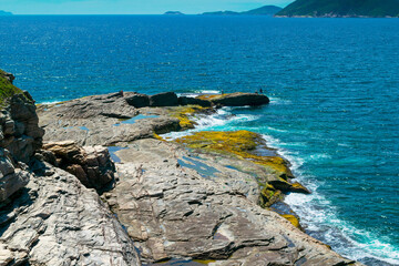 Top view of the beautiful beach of Conchas, close to the city of Cabo Frio, with blue sea around, undergrowth, large rocks and mountains in the background - 122