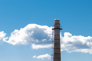A large brick chimney with a blue sky and white clouds in the background. Climate change concept,...