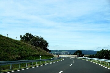 Kurvige Landstraße zwischen grüner Landschaft vor Himmel bei Sonne am Nachmittag im Sommer