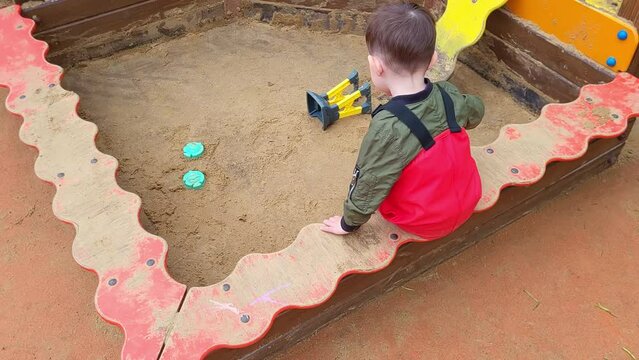 Toddler baby is playing in the sandbox on the playground. A child plays in the sand. Kid boy aged two years (two-year-old)