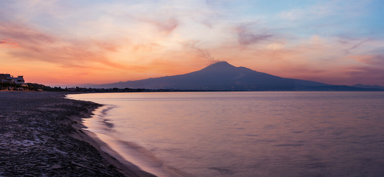 Beautiful sunset twilight on Agnone Bagni sea beach with smoky Etna volcano in far (Siracusa, Sicily, Italy). 
